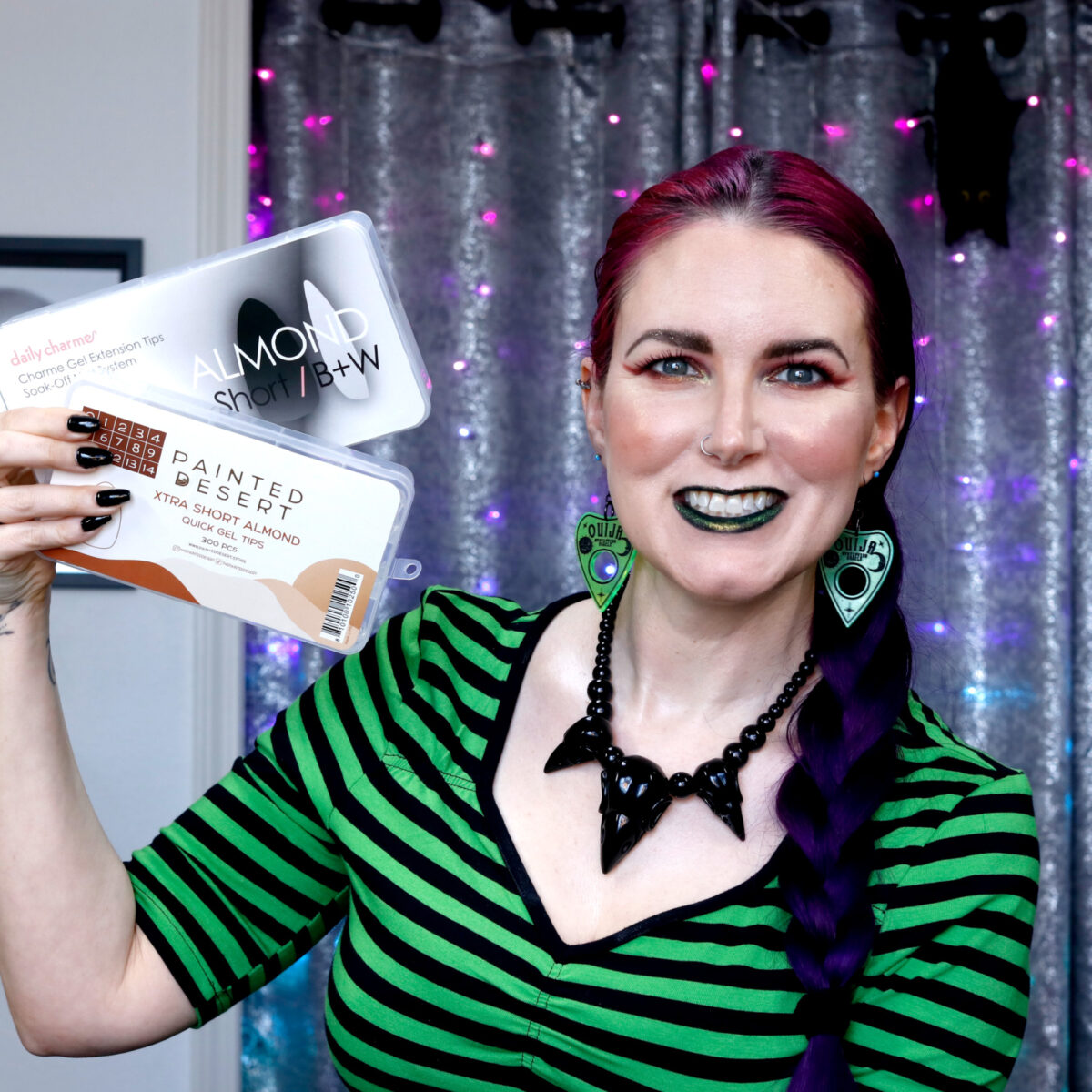 Cordelia is holding two boxes of nail art tips wearing a green and black striped shirt