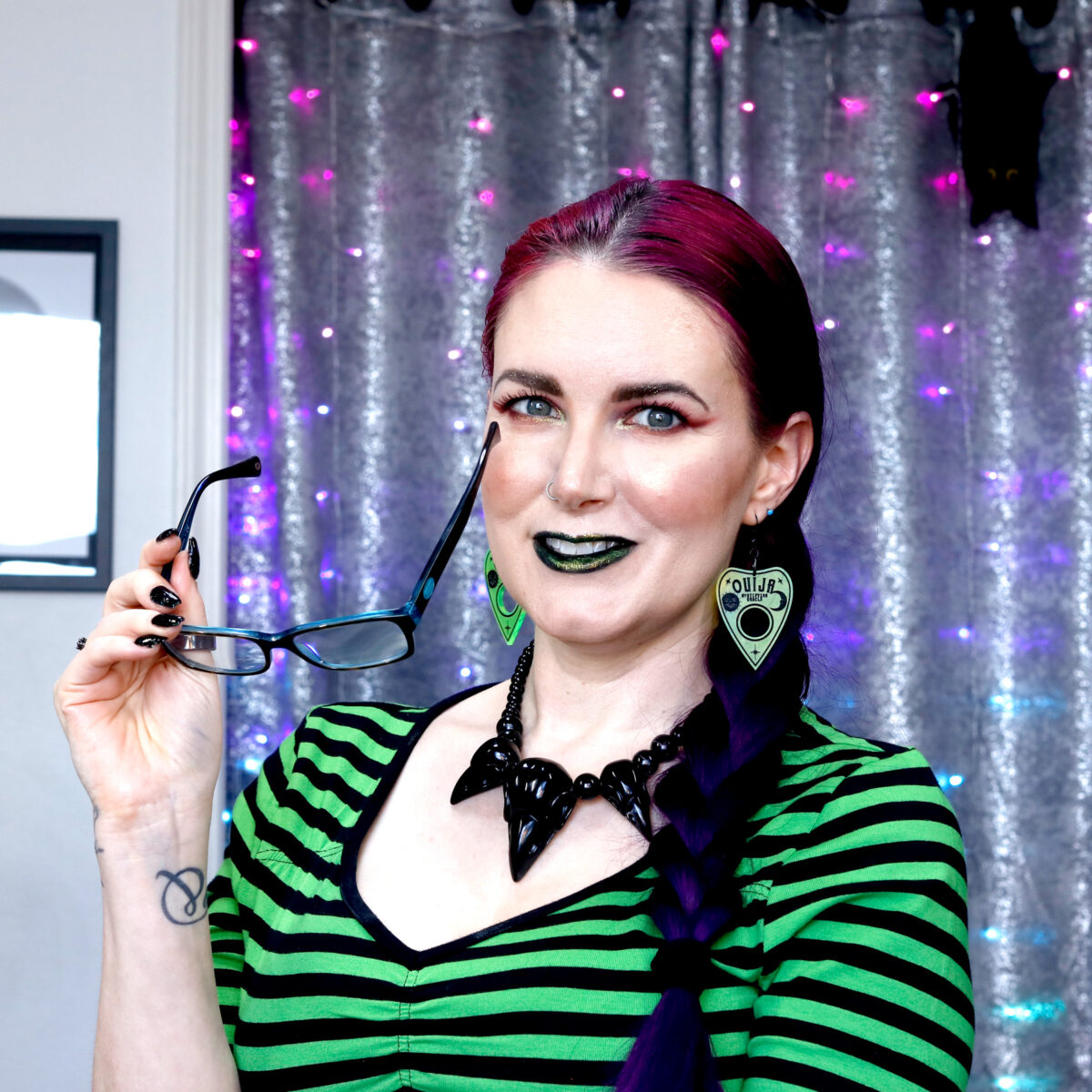 Cordelia is wearing Hell Bunny green and black striped shirt, black crow skull necklace, and green ouija planchett earrings