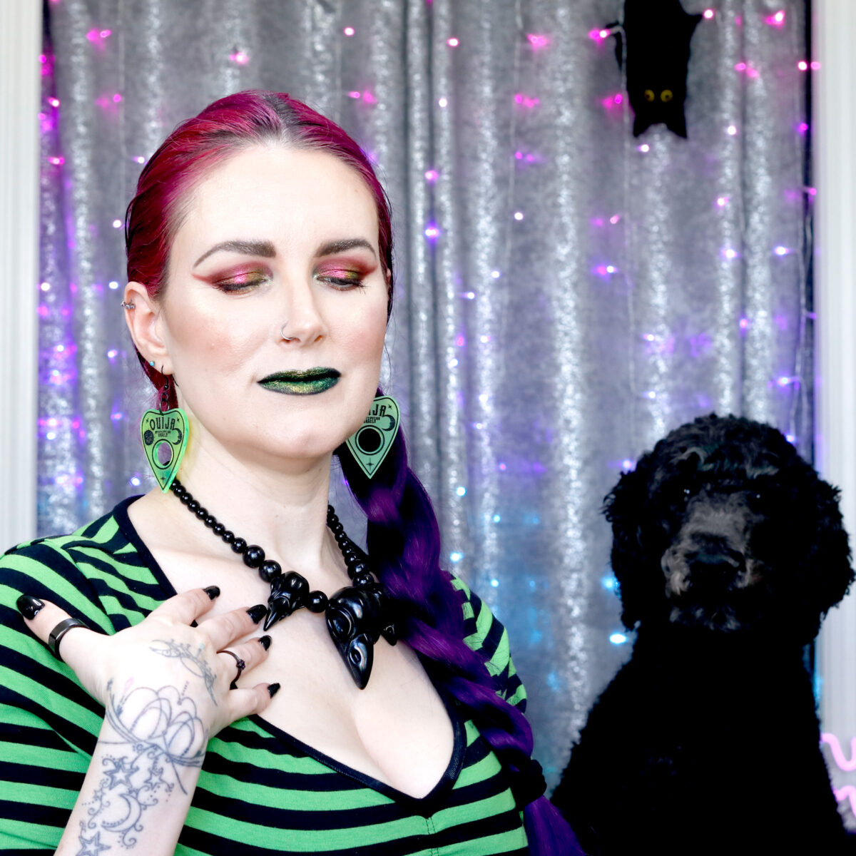 a red multichrome makeup look on Cordelia and her black dog Nyx sitting next to her
