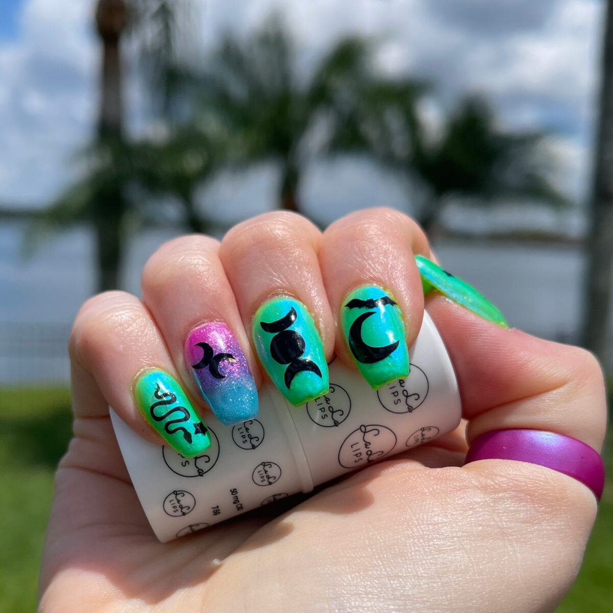 Bi Pride Nails in front of several palm trees in direct sun