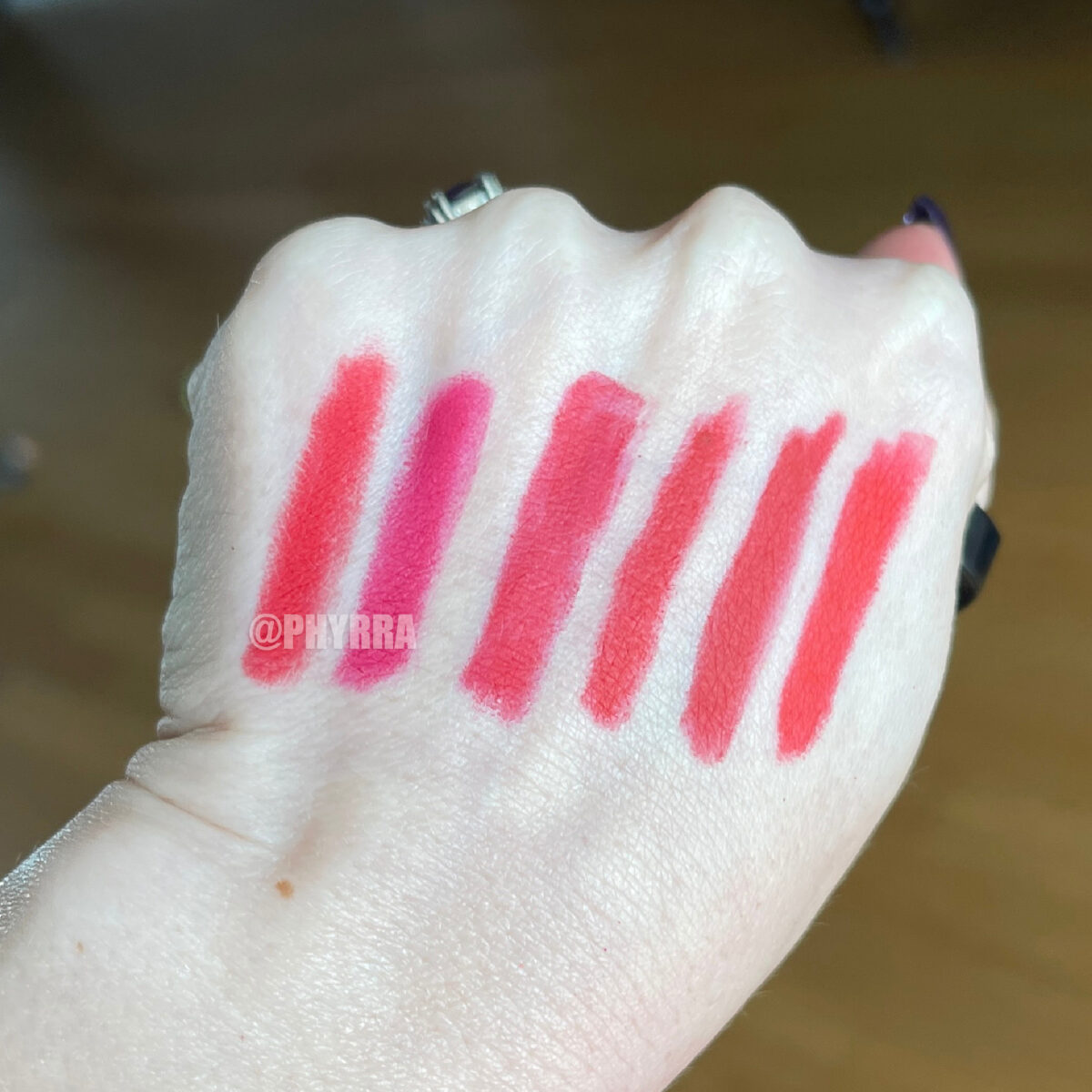 Red lip pencil swatches on pale skin indoors in indirect sunlight